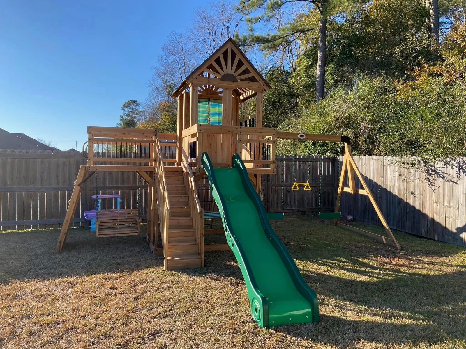 Large wooden swing set and playset with a green slide, built by Helpful Hands Assembly